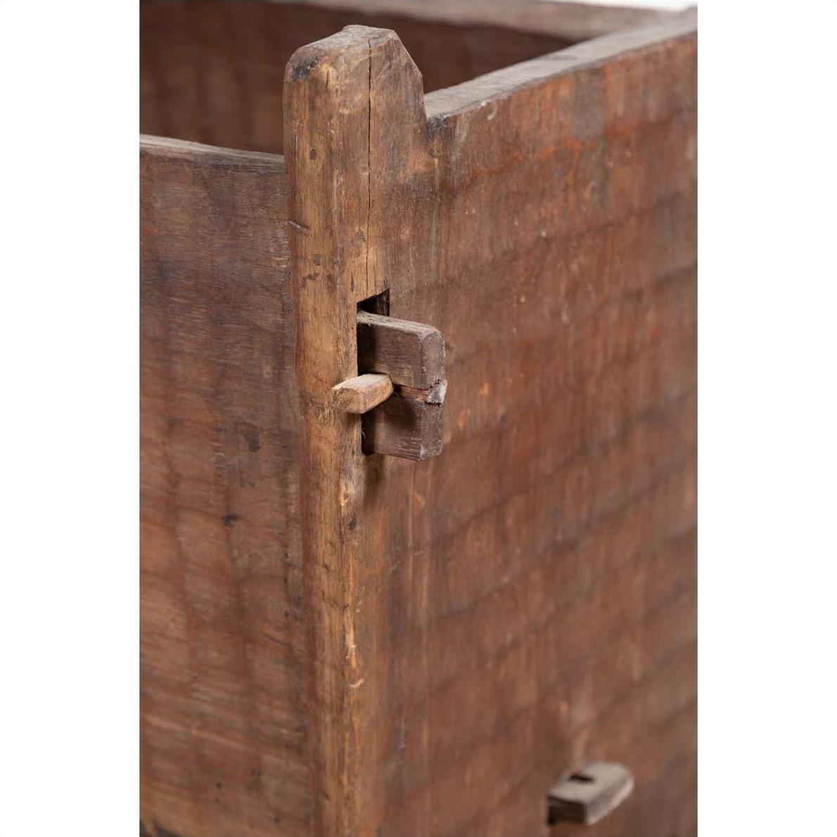 Close-up of brown weathered wood joint with peg on rustic wooden planter, showing chiseled surface texture.