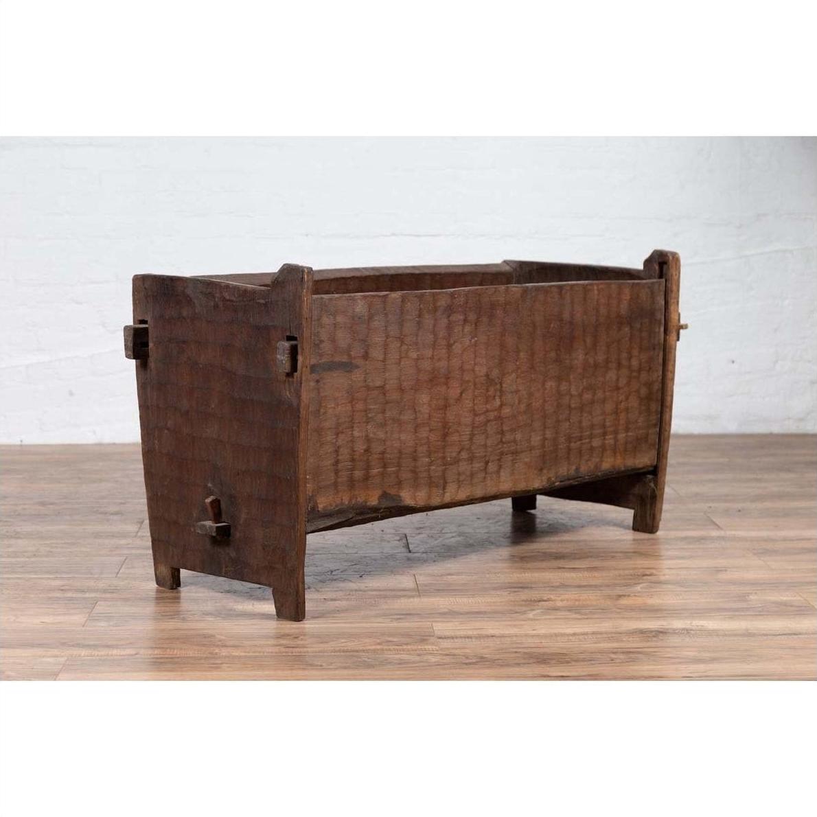 Brown weathered wood planter with chiseled texture on wooden floor.