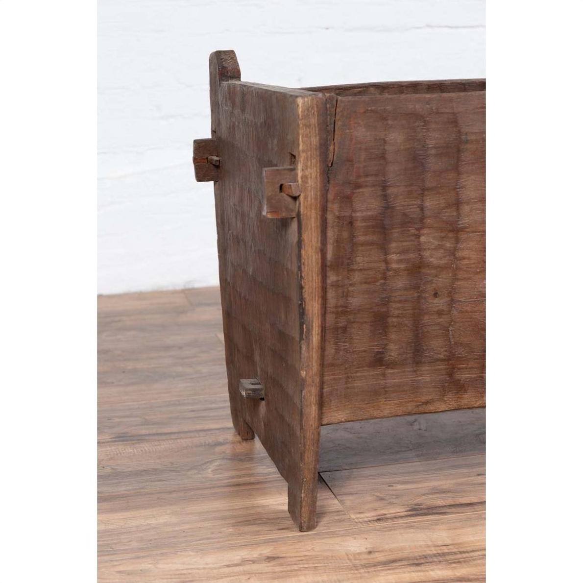 Close-up of a weathered wooden planter with chiseled texture on a wooden floor against a white wall.