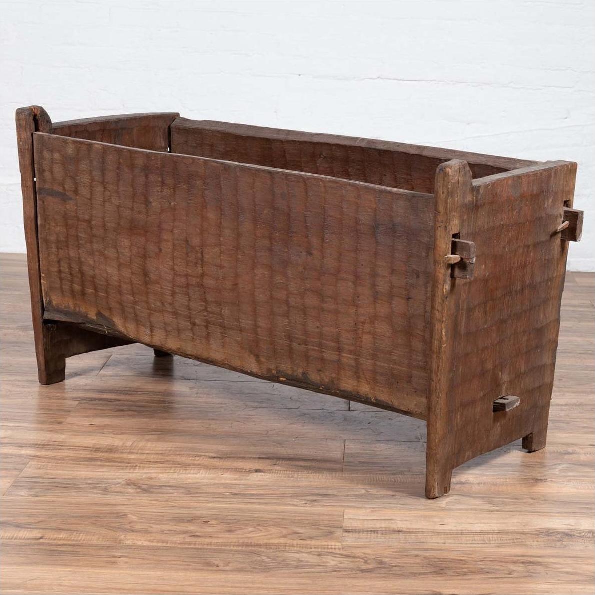 Brown weathered wooden planter with chiseled texture, open top, sitting on a wooden floor.