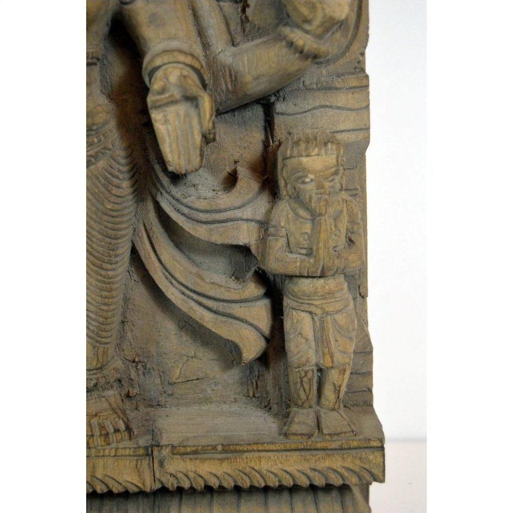 Brown Sheesham wood carving with small praying figure next to larger draped statue, close-up view.