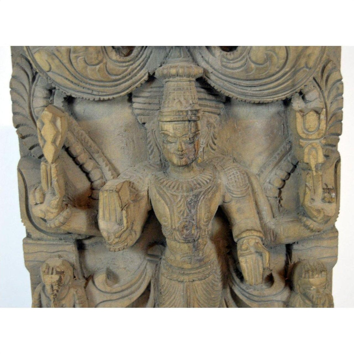 Brown Sheesham wood carving, close-up of a multi-armed deity with jewelry, headdress, and symbolic objects.