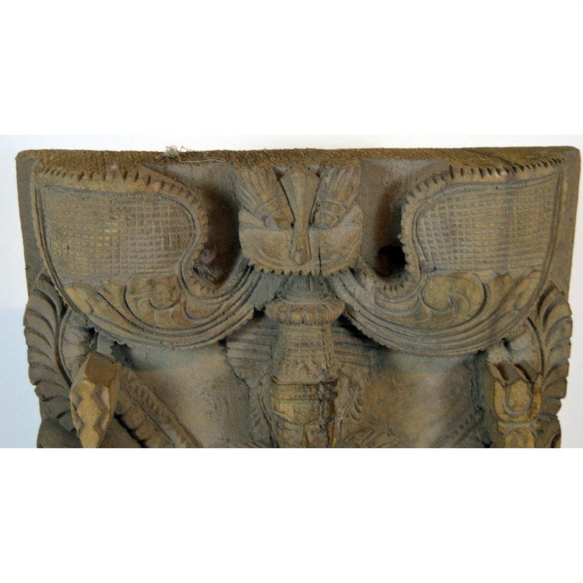 Brown sheesham wood carving sculpture close-up with intricate patterns and winged details, indoors.