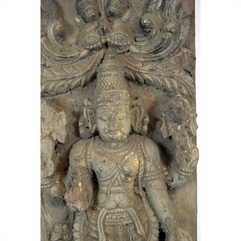 Brown Sheesham wood carving of a deity with ornate headdress, Tamil Nadu style, holding objects, close-up.