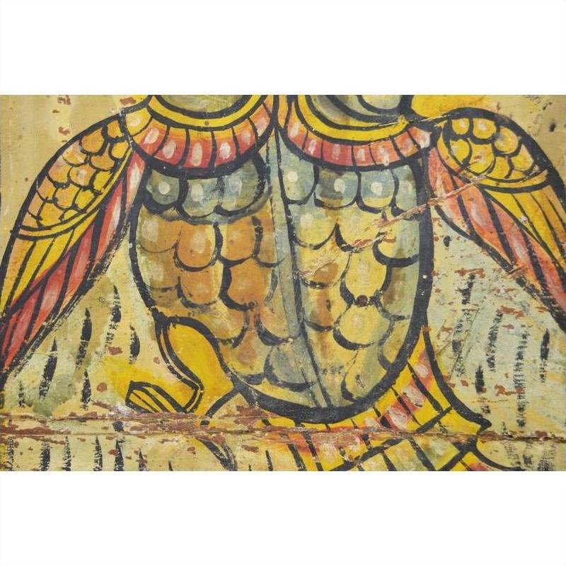 Close-up of colorful hand-painted bird wings and feathers on antique Indian wood shrine in yellow, orange, and black.