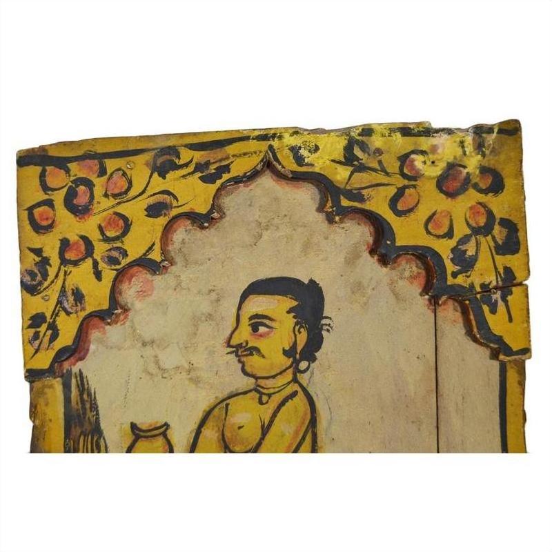 Close-up of antique Indian wood shrine with mustached man under arch, yellow and red floral accents, New Delhi origin.