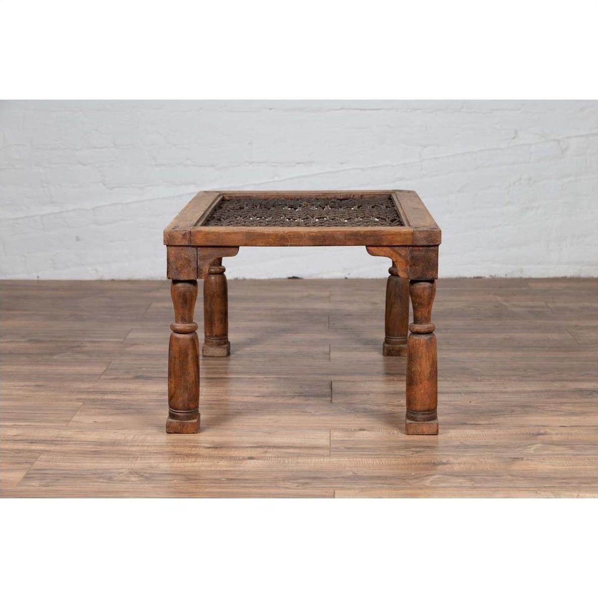 Brown wooden side table with window grate design and turned baluster legs on a wooden floor indoors.