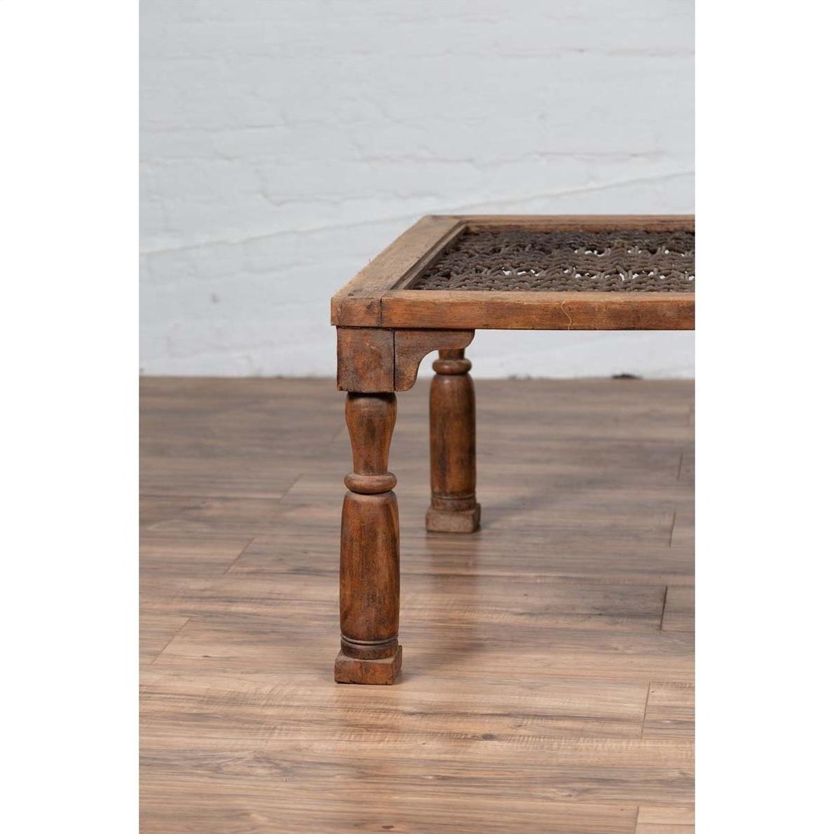 Close-up of brown wooden side table with window grate and turned baluster legs on wood floor by white brick wall.