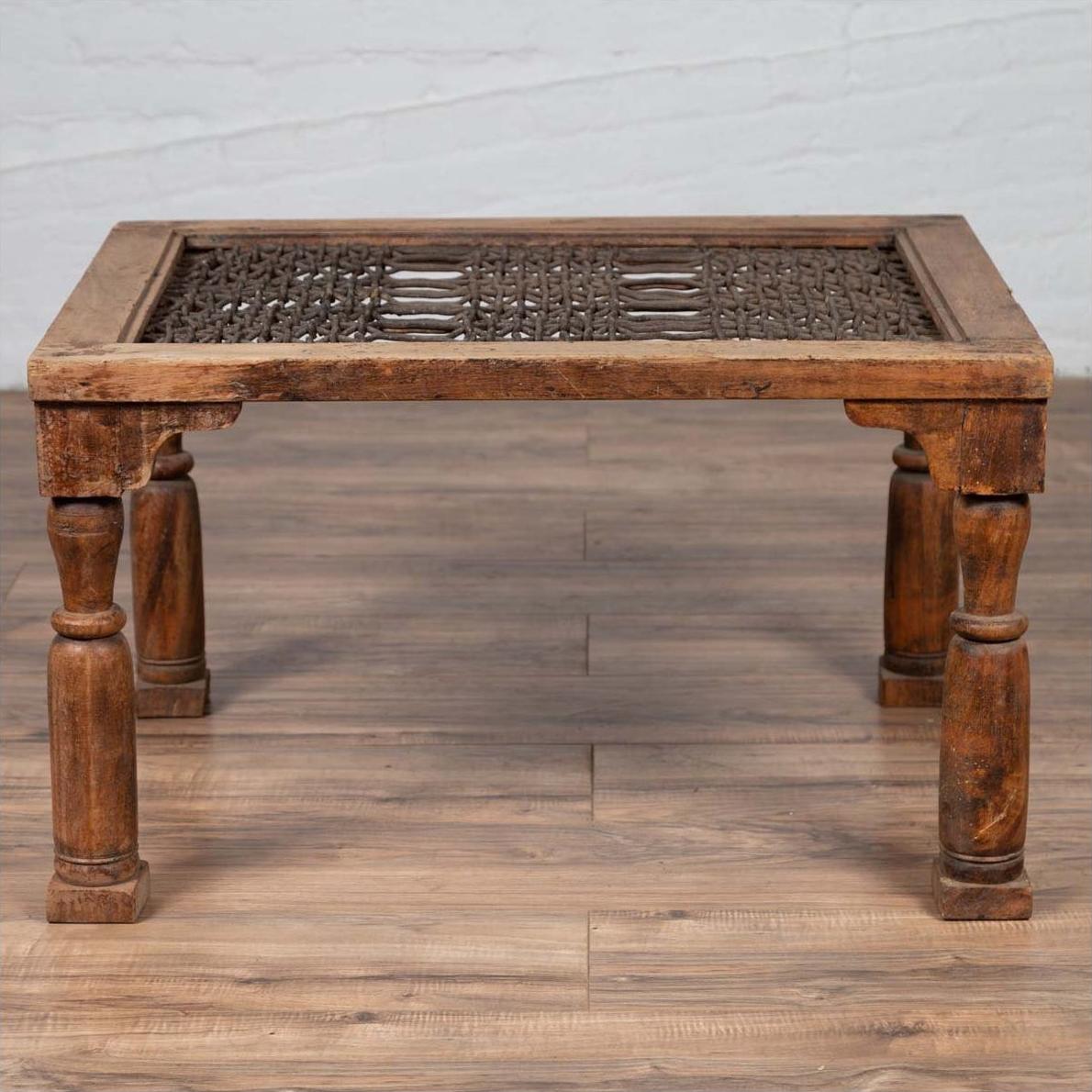 Brown wooden side table with window grate top and turned baluster legs on a wooden floor indoors.