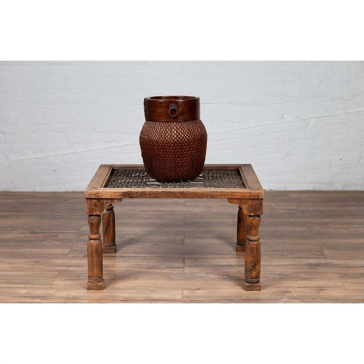 Brown wooden side table with window grate top and baluster legs against a white brick wall indoor setting.