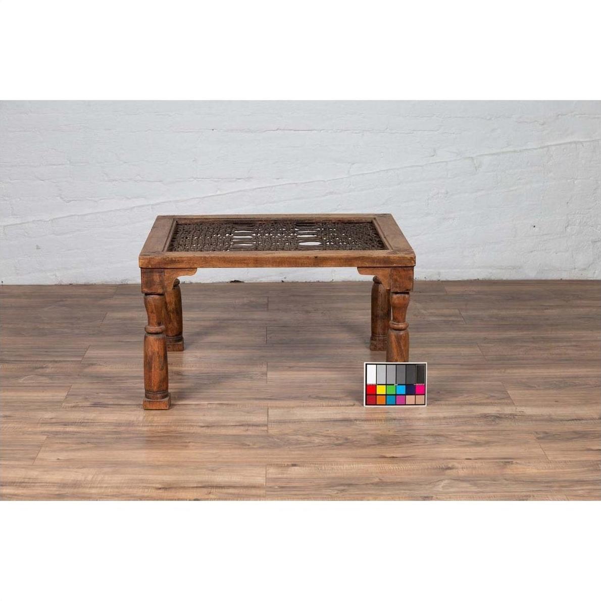 Brown wooden side table with window grate and baluster legs on wooden floor near a color chart.