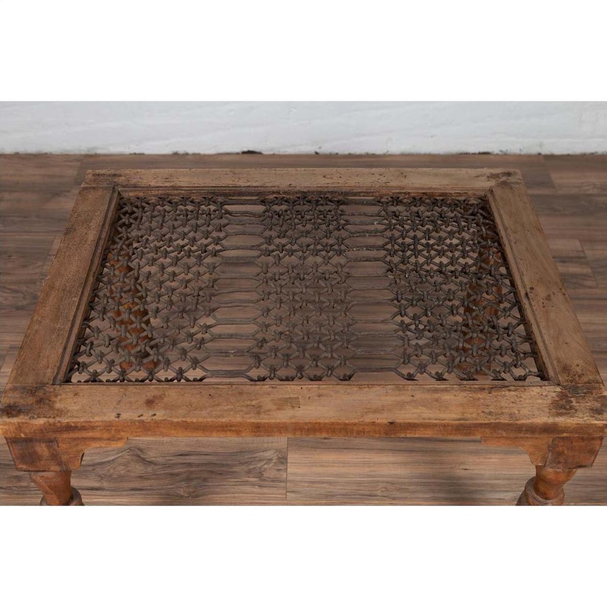 Brown wooden side table with window grate top and turned baluster legs on a wood floor against a white wall indoors.