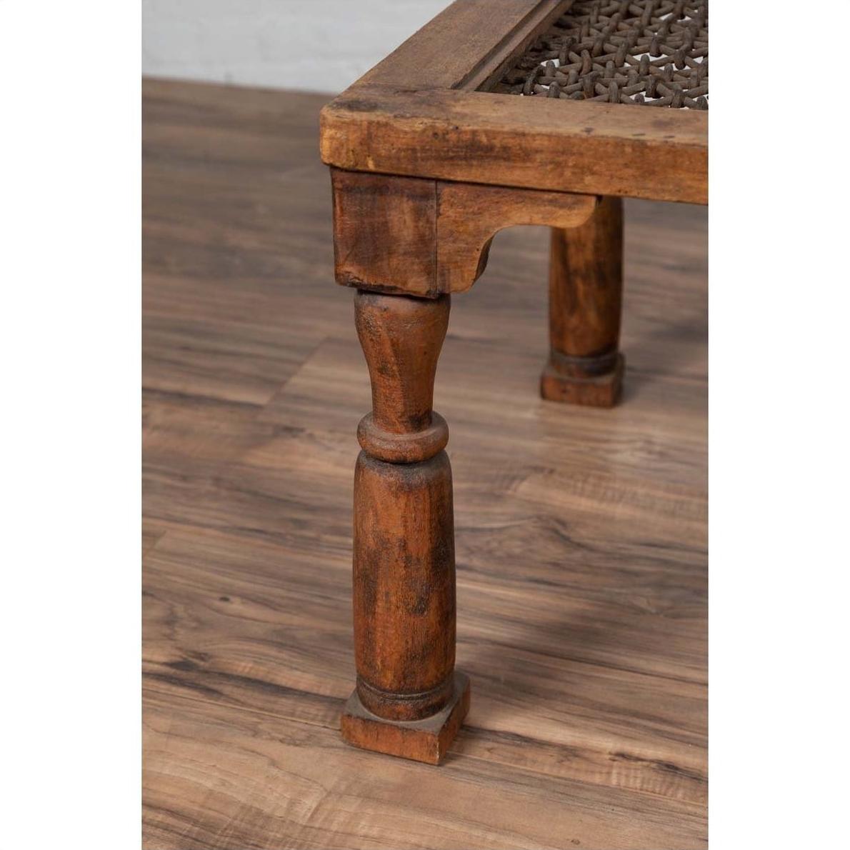 Close-up of brown wooden Indian side table with window grate detail and turned legs on a wooden floor.