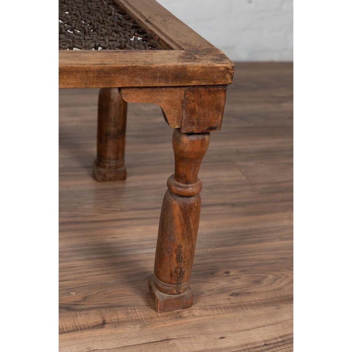 Close-up of brown wooden side table leg with carved details, on wood floor with woven tabletop partly visible.
