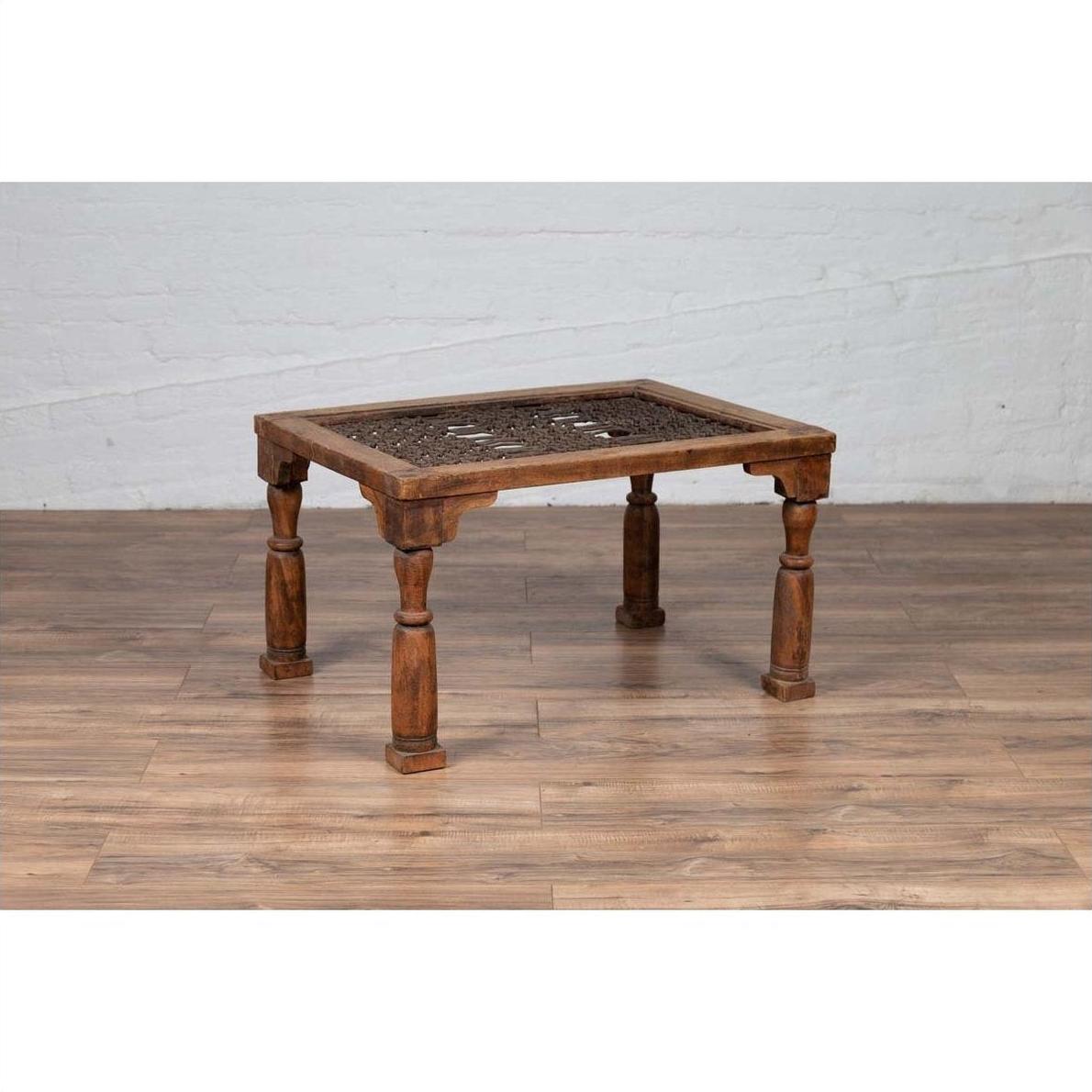Brown wooden side table with window grate top and turned baluster legs on a wood floor against a brick wall.