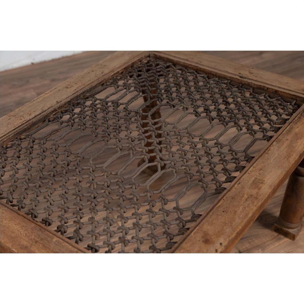 Brown wooden side table with window grate top and turned baluster legs on wood floor, indoors.