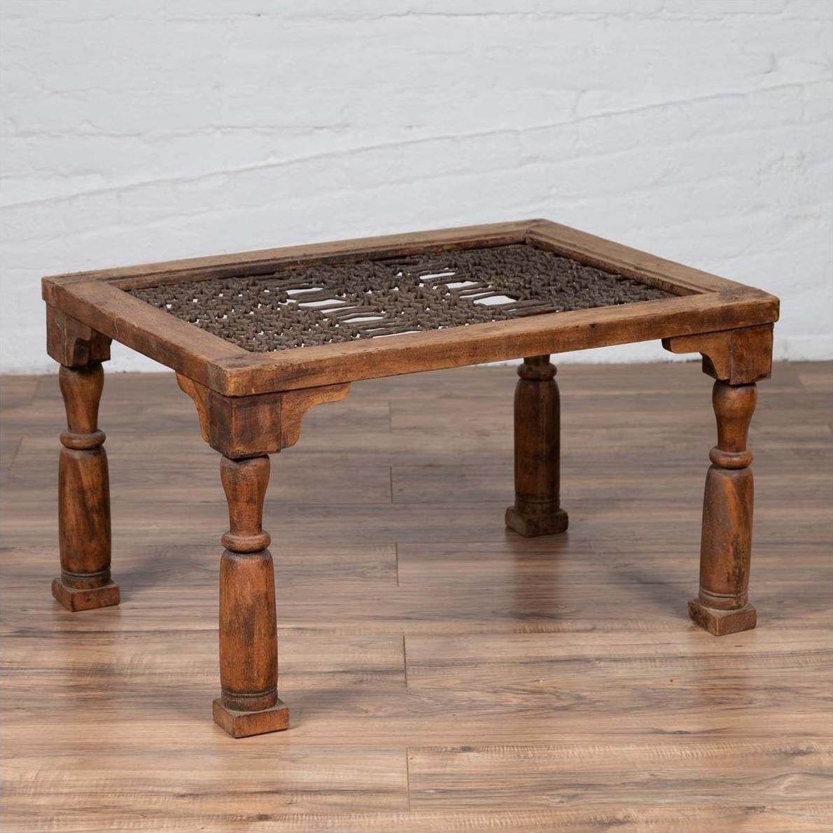 Brown wooden Indian side table with window grate top and turned baluster legs on wooden floor against white wall.