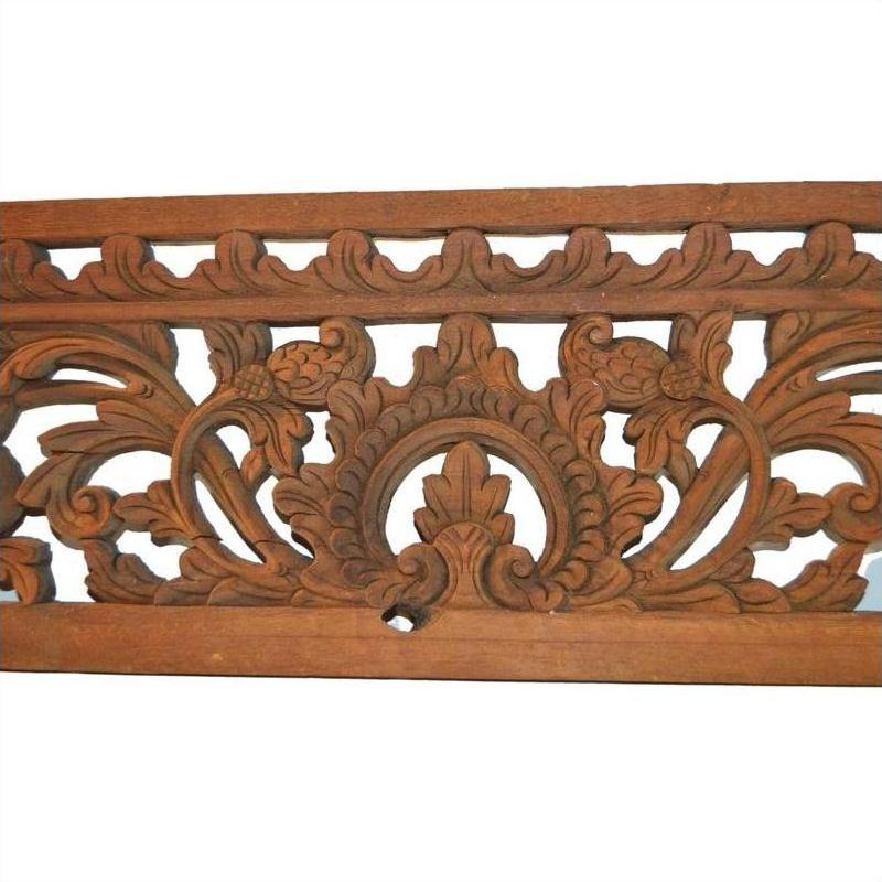 Brown wood Indonesian carving with intricate, symmetrical floral and leaf patterns, close-up wall decor detail.