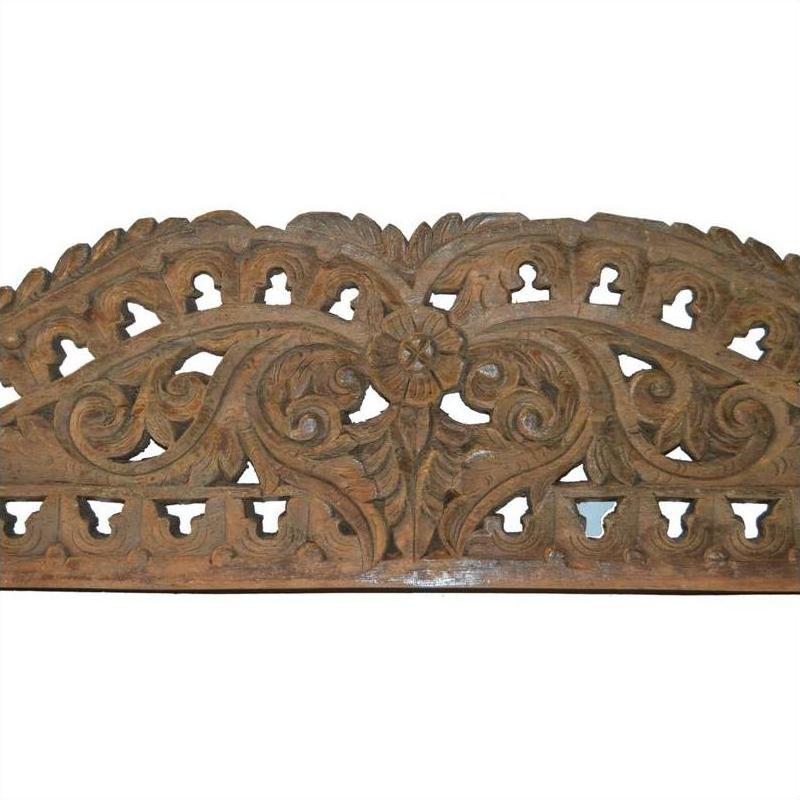 Brown wood Indonesian wall carving with intricate floral and vine cut-out designs, close-up view.