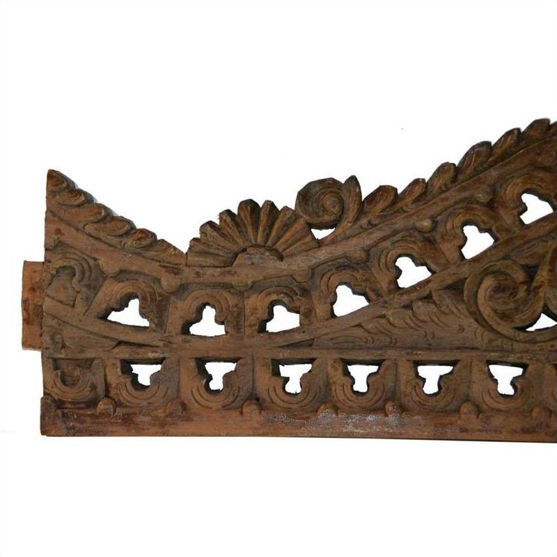 Brown wood Indonesian wall carving with intricate floral scroll patterns, geometric cutouts, and rustic finish, close-up.