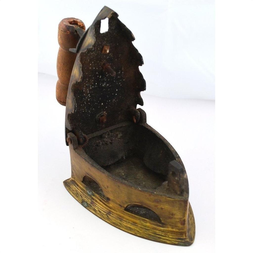 Close-up of antique Indonesian coal iron with a wooden handle and open lid, metal body, on plain background.
