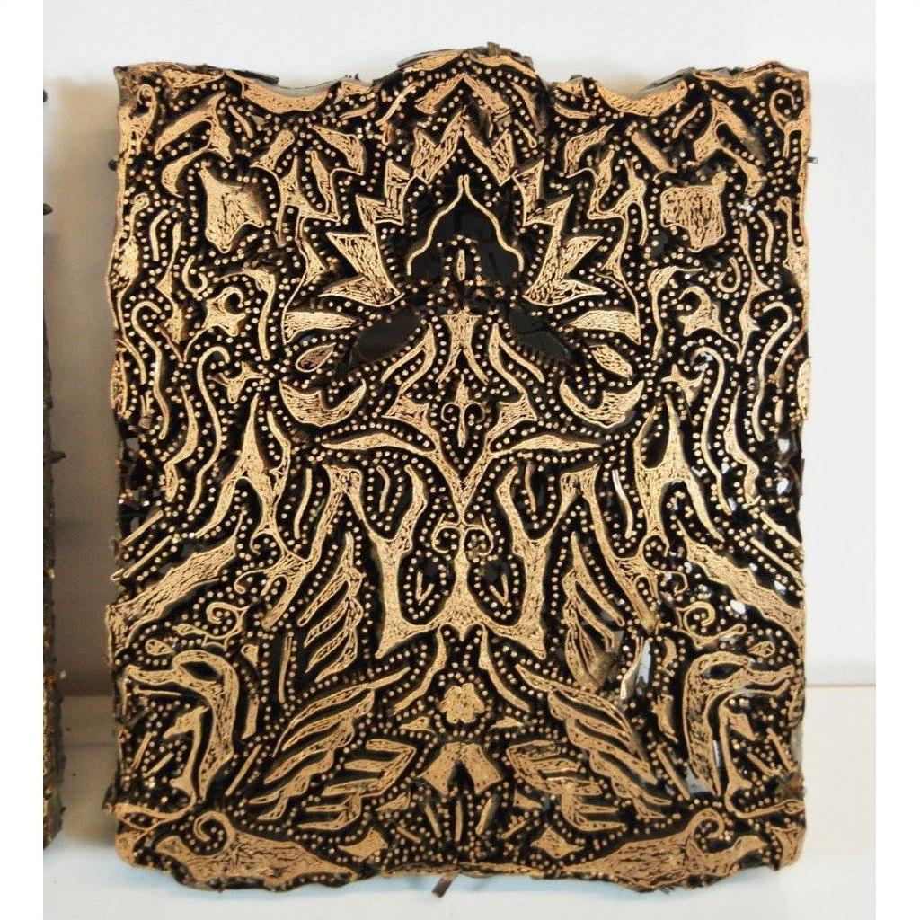Close-up of three black and gold antique Indonesian copper batik ink blocks with symmetrical floral patterns.