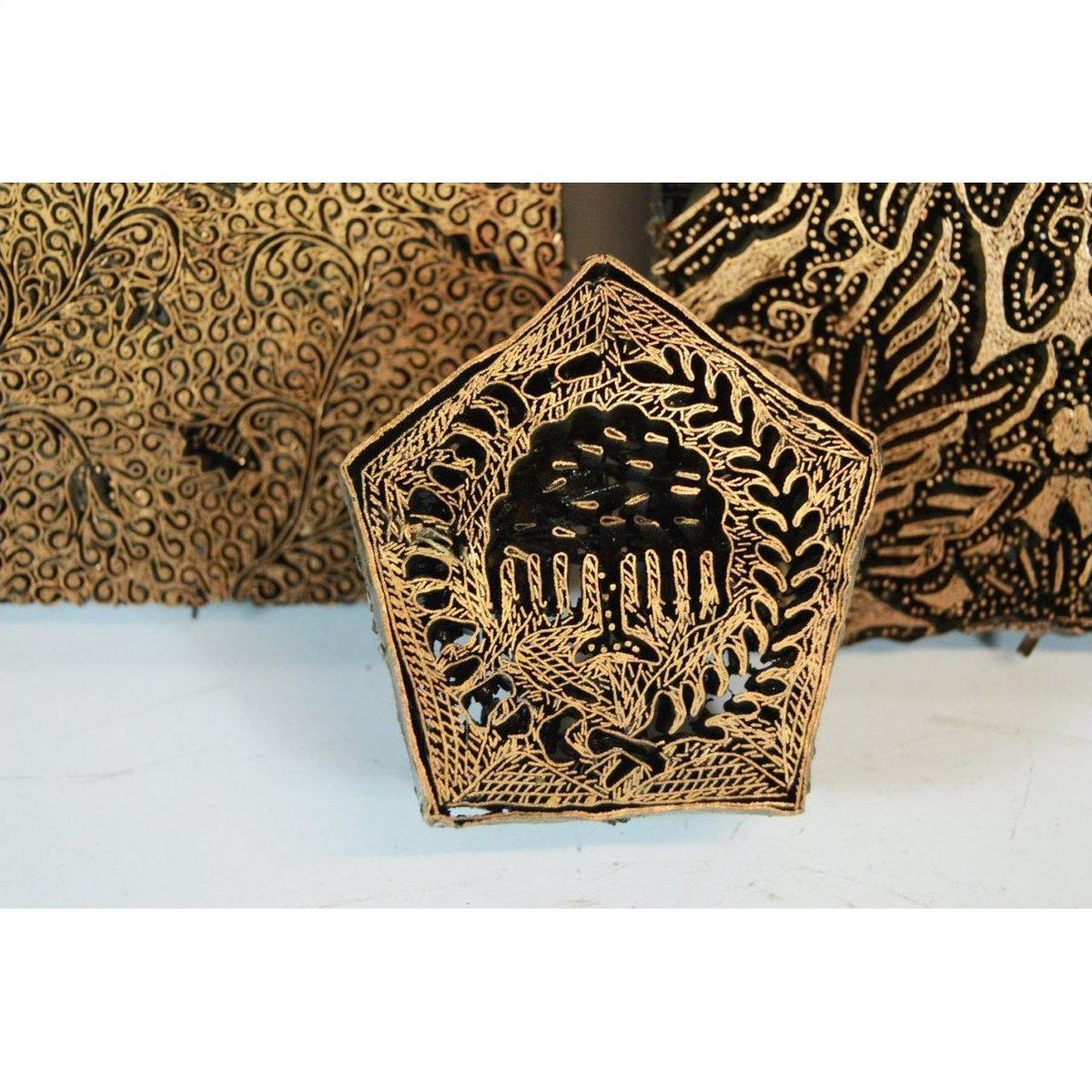 Close-up of three antique copper batik ink blocks with intricate floral and leaf carvings, Indonesian textile tools.
