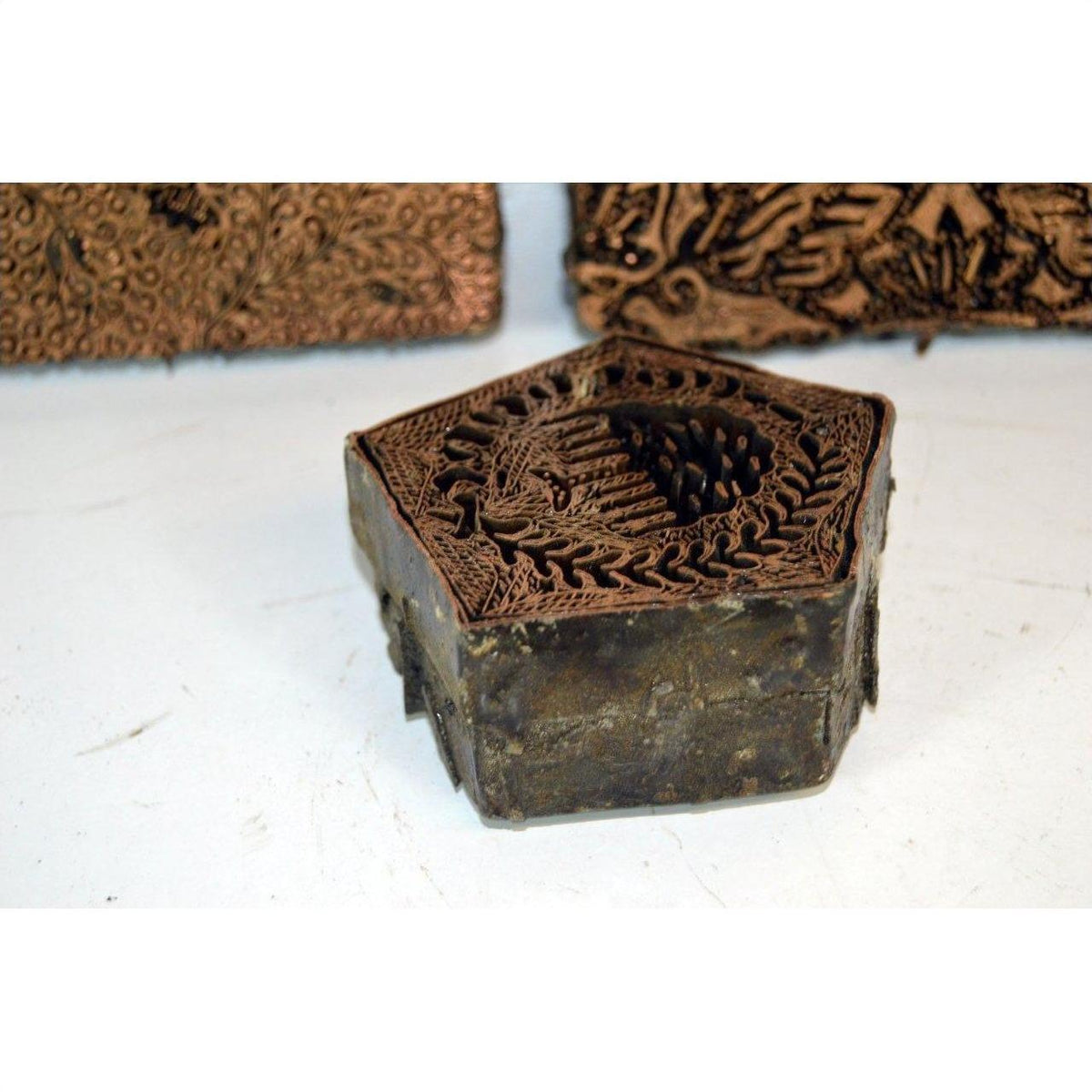 Copper batik ink blocks set with intricate floral and bird designs, close-up on white surface.