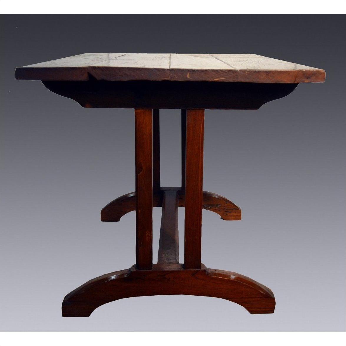 Brown teakwood dining table with thick plank top and sturdy curved legs, shown from the side.