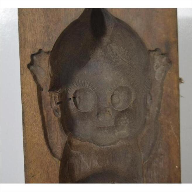 Brown wooden antique Indonesian mold with hand carved cartoon baby, large eyes, and raised arms, close-up view.