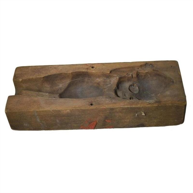 Brown wooden mold with hand-carved top view of a lying baby or child, antique Indonesian craftsmanship, close-up.