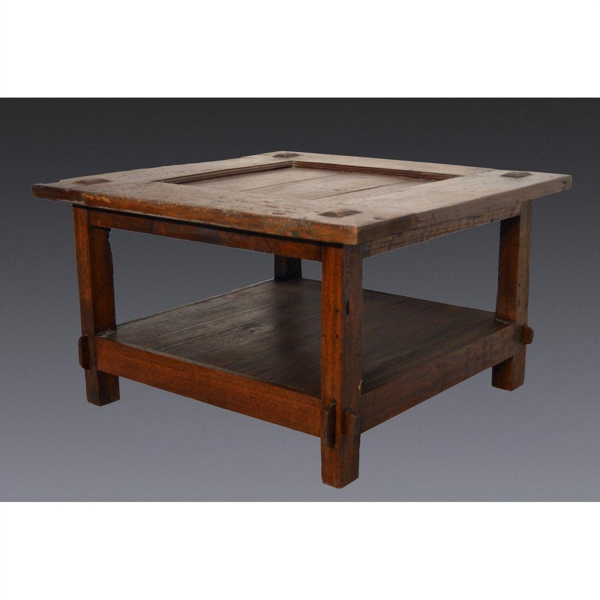 Brown wooden Indonesian table with lower shelf, Dutch Colonial style, on plain gray background.