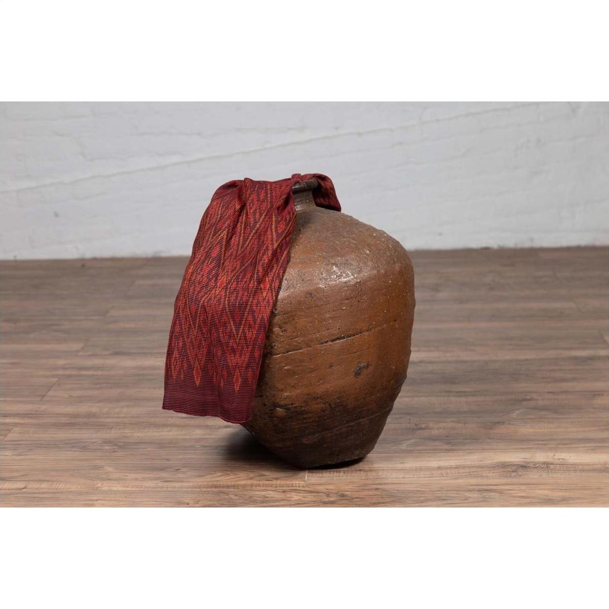 Close-up of an antique Japanese brown oil jar with a weathered, irregular shape on a wooden floor.