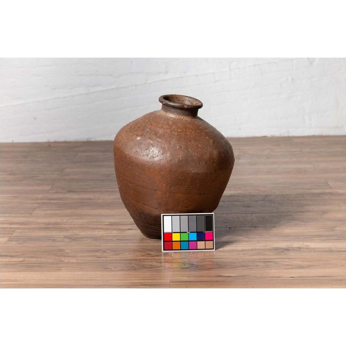 Brown ceramic Japanese oil jar with weathered, irregular shape on wooden floor, color calibration card in front.