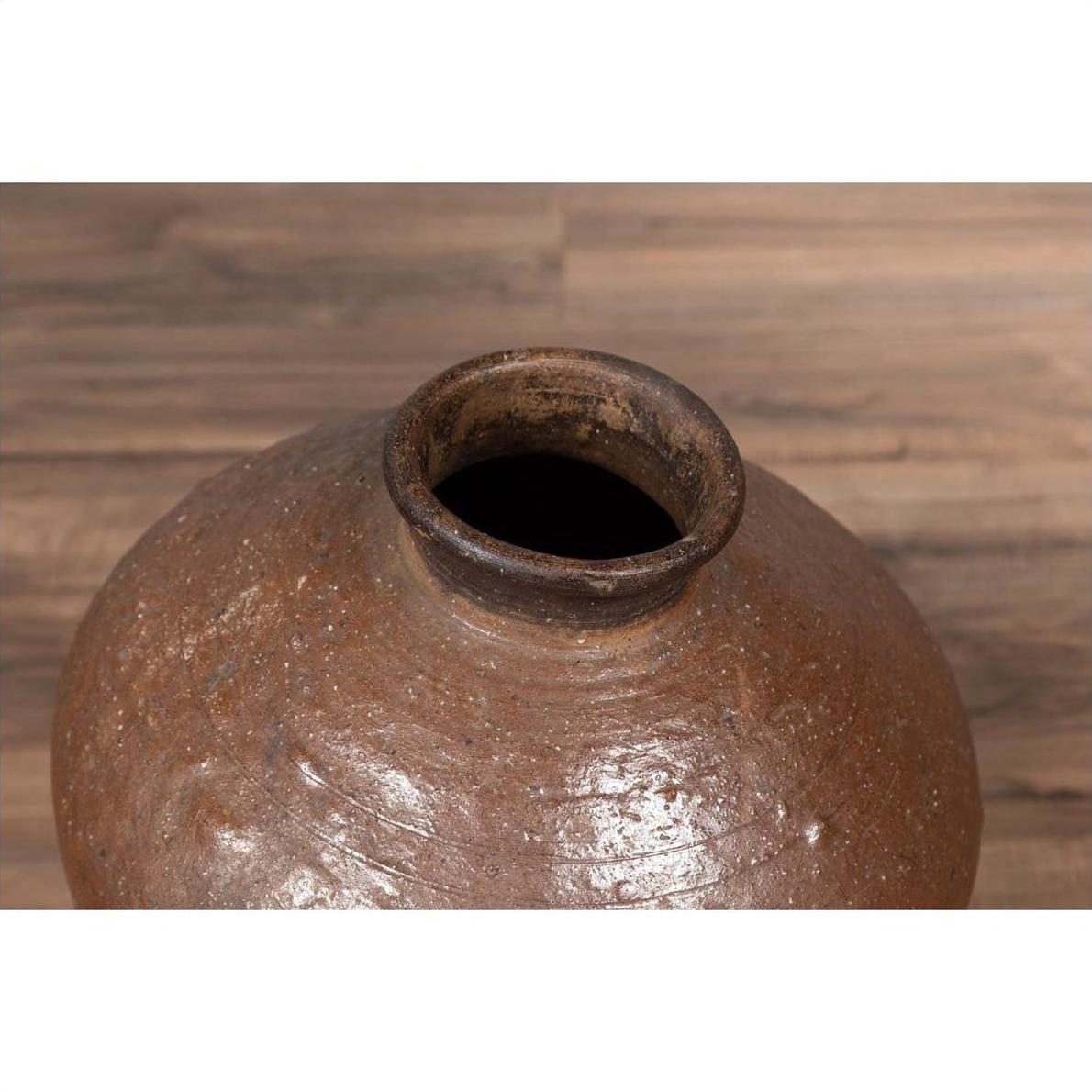 Close-up of antique Japanese brown ceramic oil jar with weathered, irregular shape and narrow opening on wood surface.