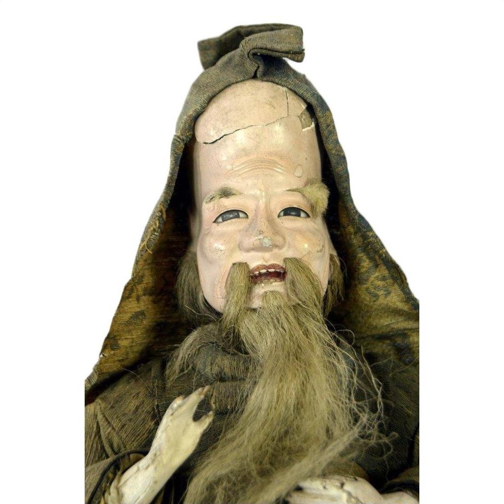 Close-up of antique Japanese Edo samurai doll in old fabric clothes, tall hat, long beard, cracked forehead, missing feet.