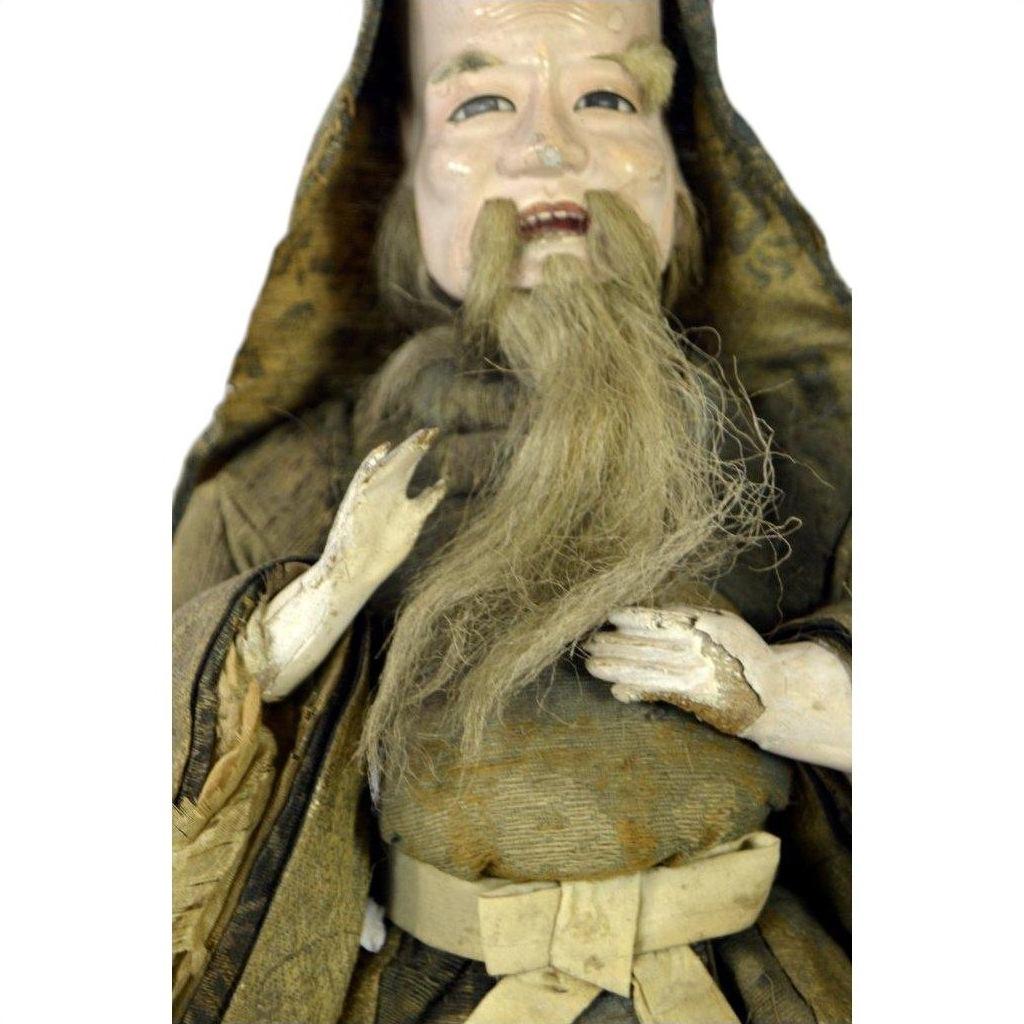Close-up of an antique Japanese Edo Samurai doll with long gray beard, smiling face, and brown hooded robe.
