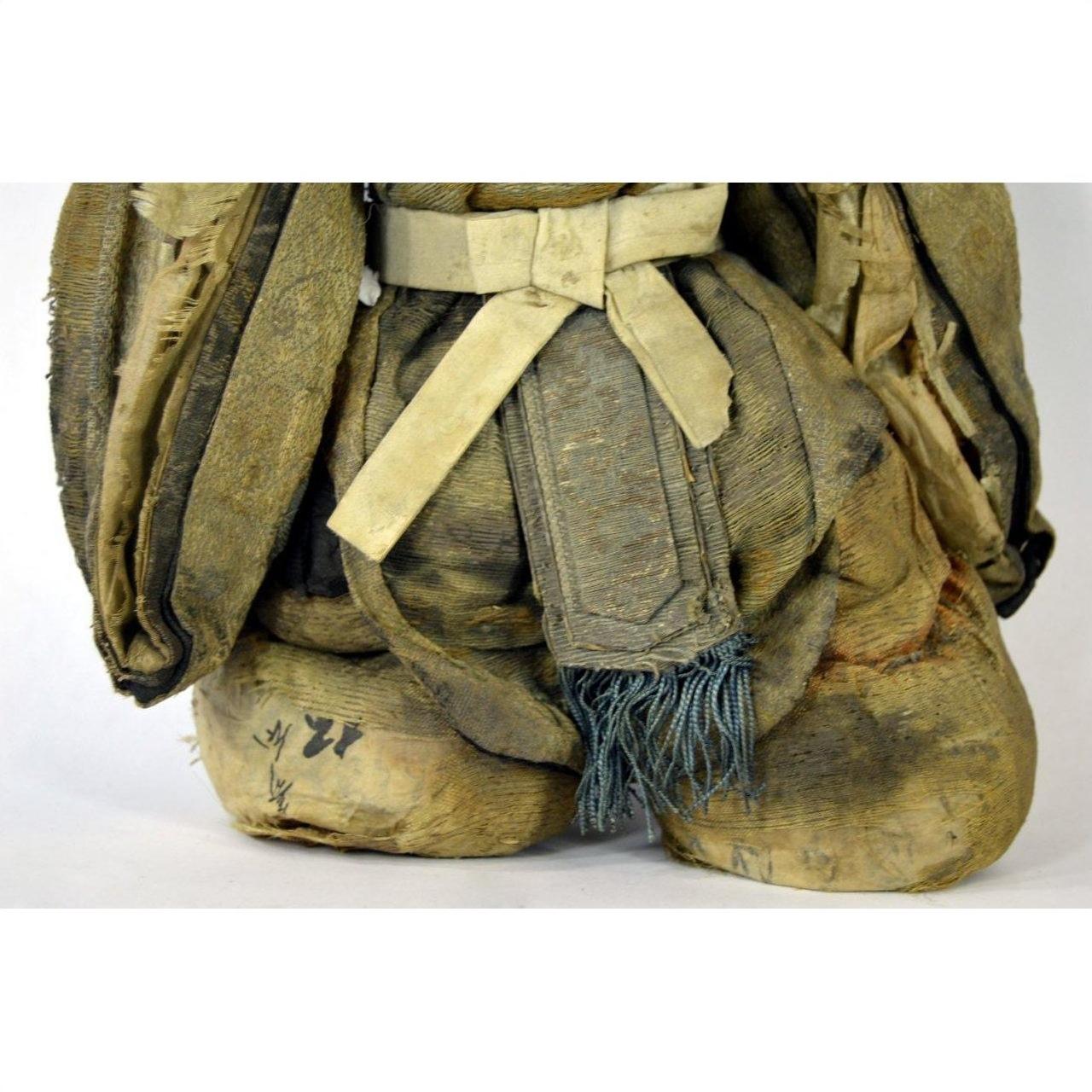 Close-up of an antique Japanese Edo samurai doll in faded fabric clothing with frayed edges and visible stitching.