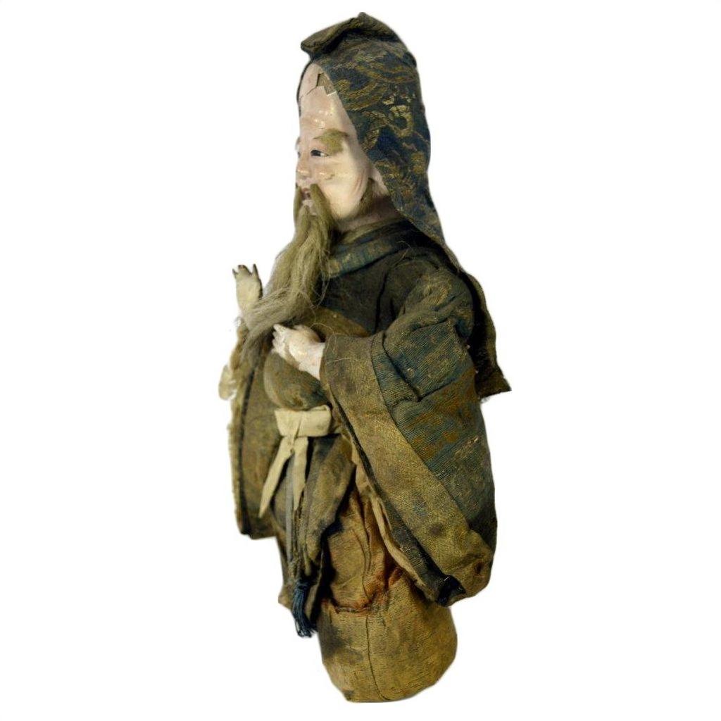 Close-up of antique Japanese Edo samurai doll in patterned kimono with hood and beard, aged fabric, missing feet, on white.