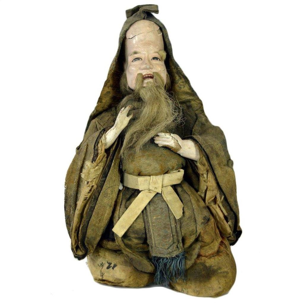 Close-up of antique bearded Japanese Edo Samurai doll in worn brown hooded robe, kneeling, missing feet.