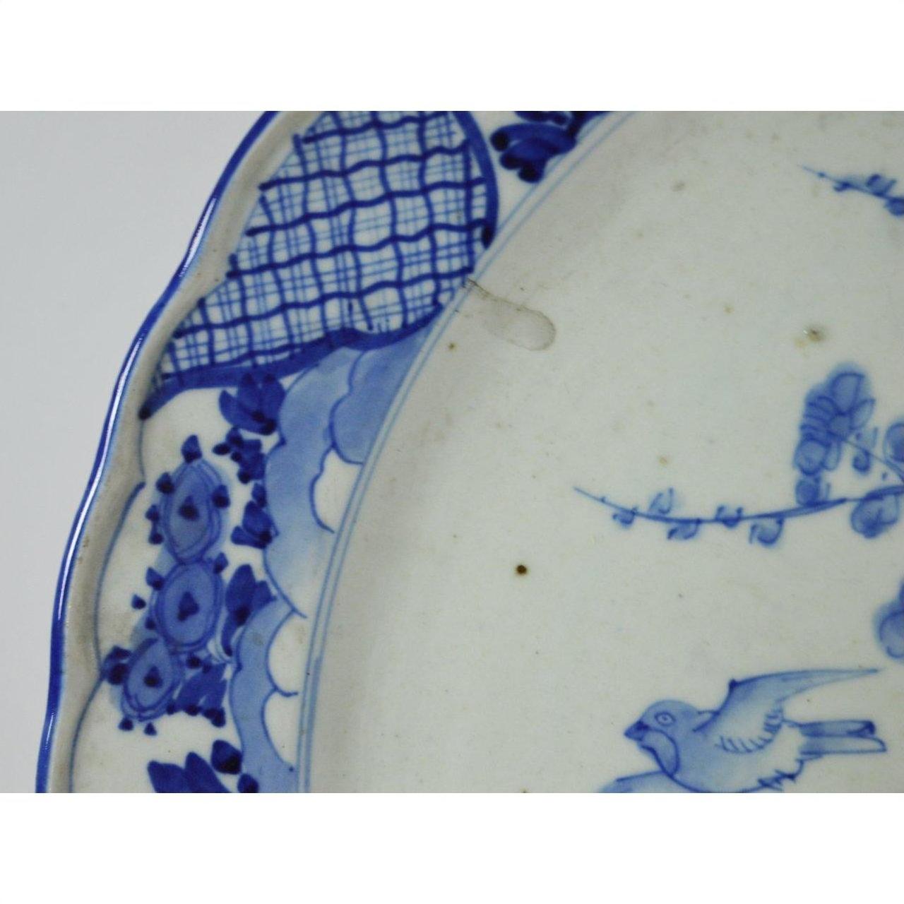 Blue and white ceramic plate with hand painted floral patterns and a bird near the edge, close-up.
