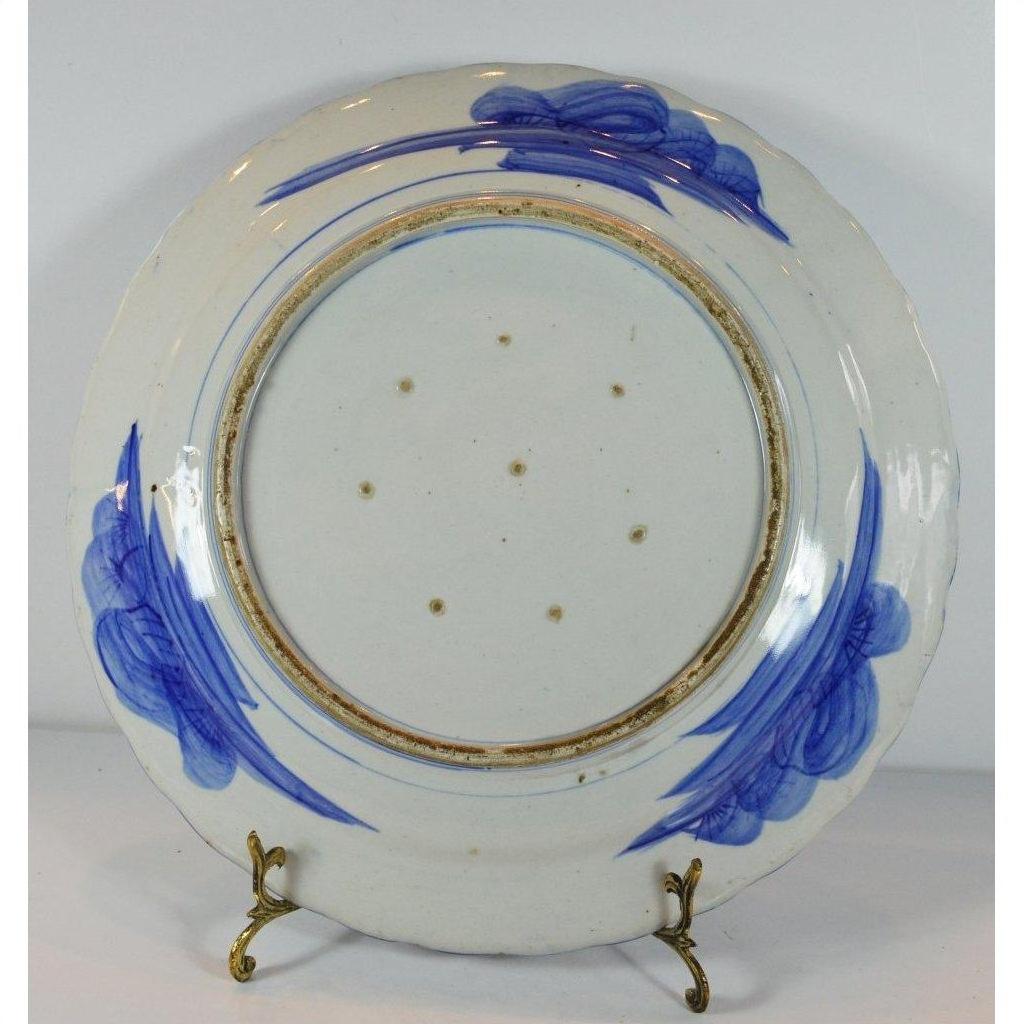 Blue and white ceramic Japanese plate with hand-painted brushstrokes and small holes, on a brass stand.