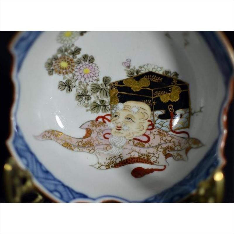 Close-up of antique Japanese porcelain bowl with hand painted old man, chest, flowers, and gold-blue detailing.