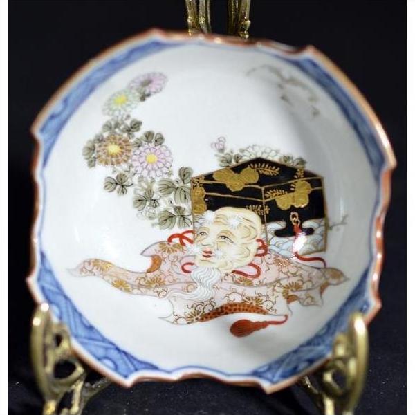Antique Japanese porcelain dish, hand painted, white with patterns, placed beside a black and gold chest on a surface.