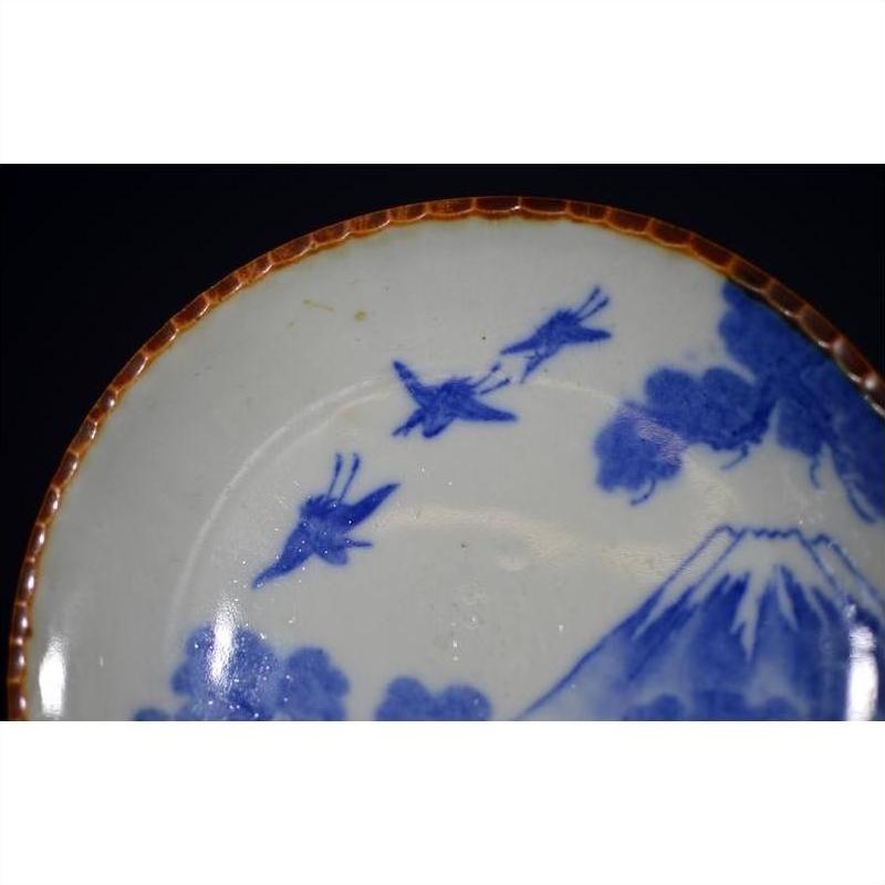 Close-up of brown-rimmed ceramic Japanese Igezara transferware plate with blue birds, clouds, and Mt. Fuji motif.
