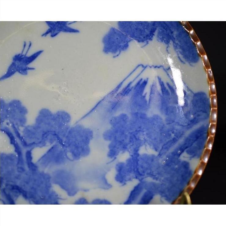 Blue and white ceramic Igezara transferware plate with mountain, trees, birds, and gold rim, close-up view.