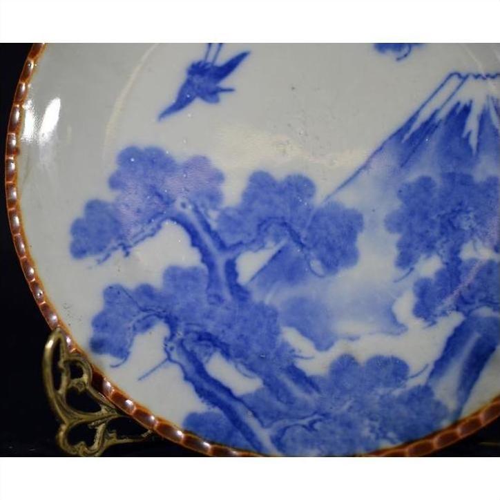 Blue and white ceramic Igezara transferware plate with tree, mountain, and bird design on ornate gold stand.
