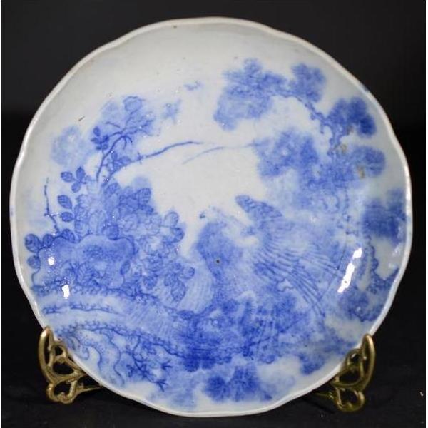 Blue and white ceramic Igezara transferware plate with floral and bird pattern on stand against a dark background.