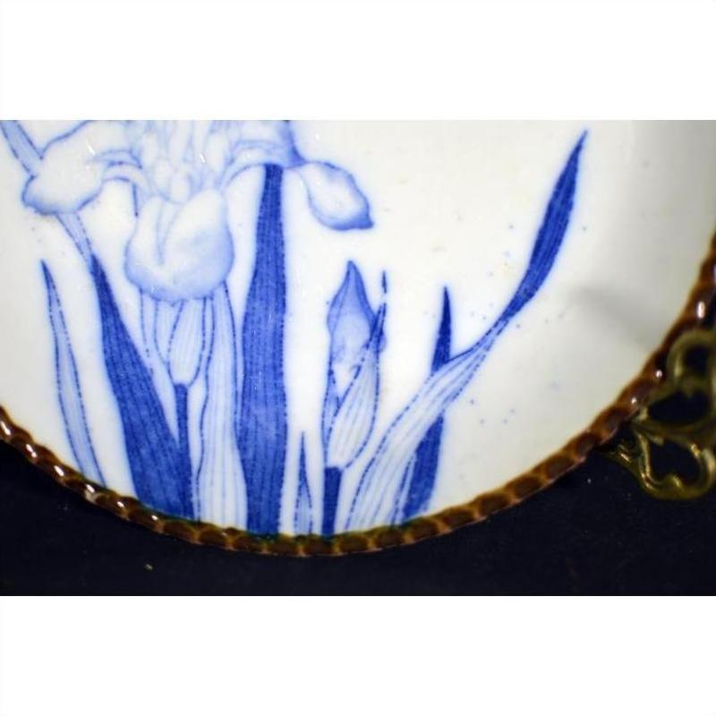 Close-up of blue floral pattern on white porcelain Igezara plate with brown textured rim, against black background.