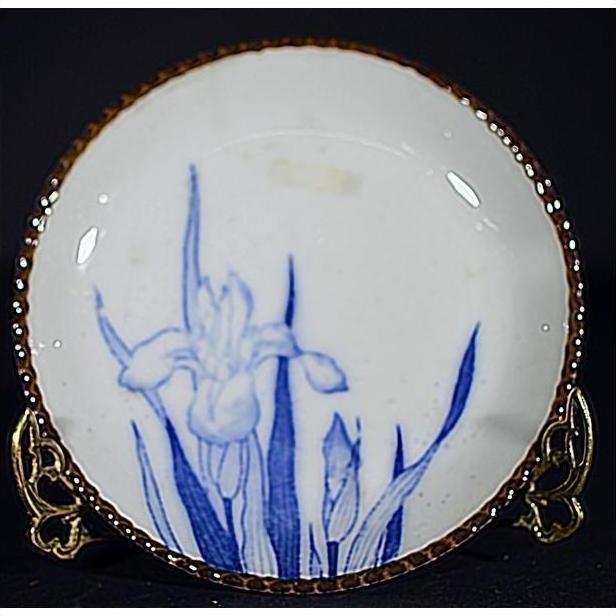 Blue and white ceramic Igezara transferware plate with iris design on ornate metal stand, dark background.